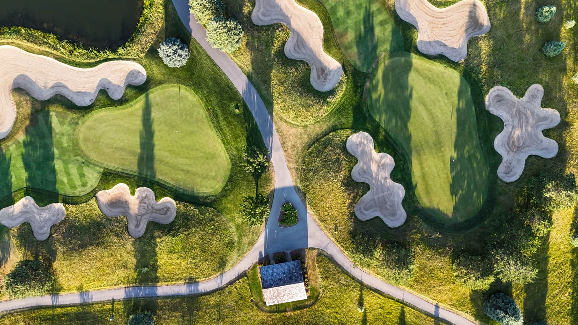 Top-down aerial of two greens at The Fortress, clean-edged sand bunkers and golden fescue mounds divided by cart paths