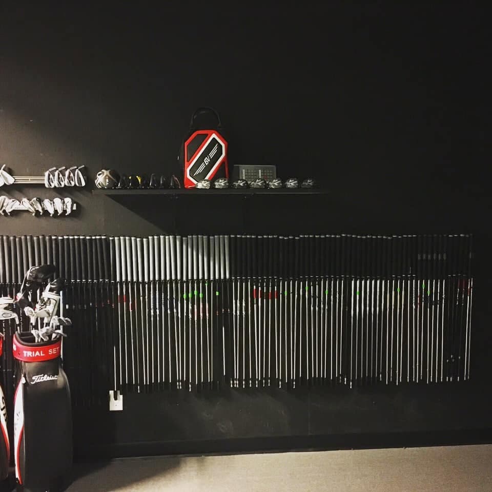 Iron heads and fitting shafts racked in the Trackman Studio, a Titleist trial-set bag beside them