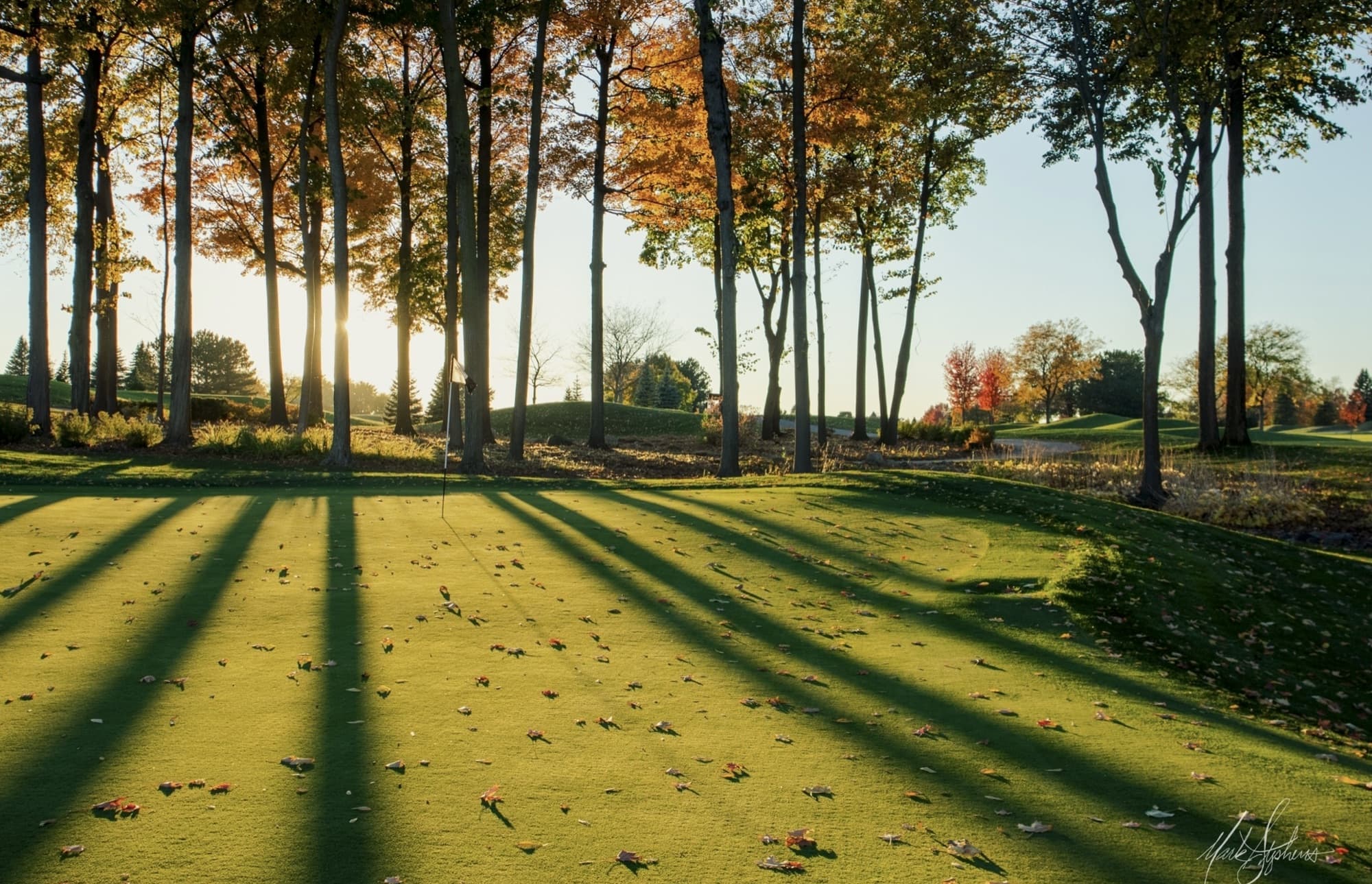Ground-level view of a green at The Fortress at sunset, long shadows from backlit trees