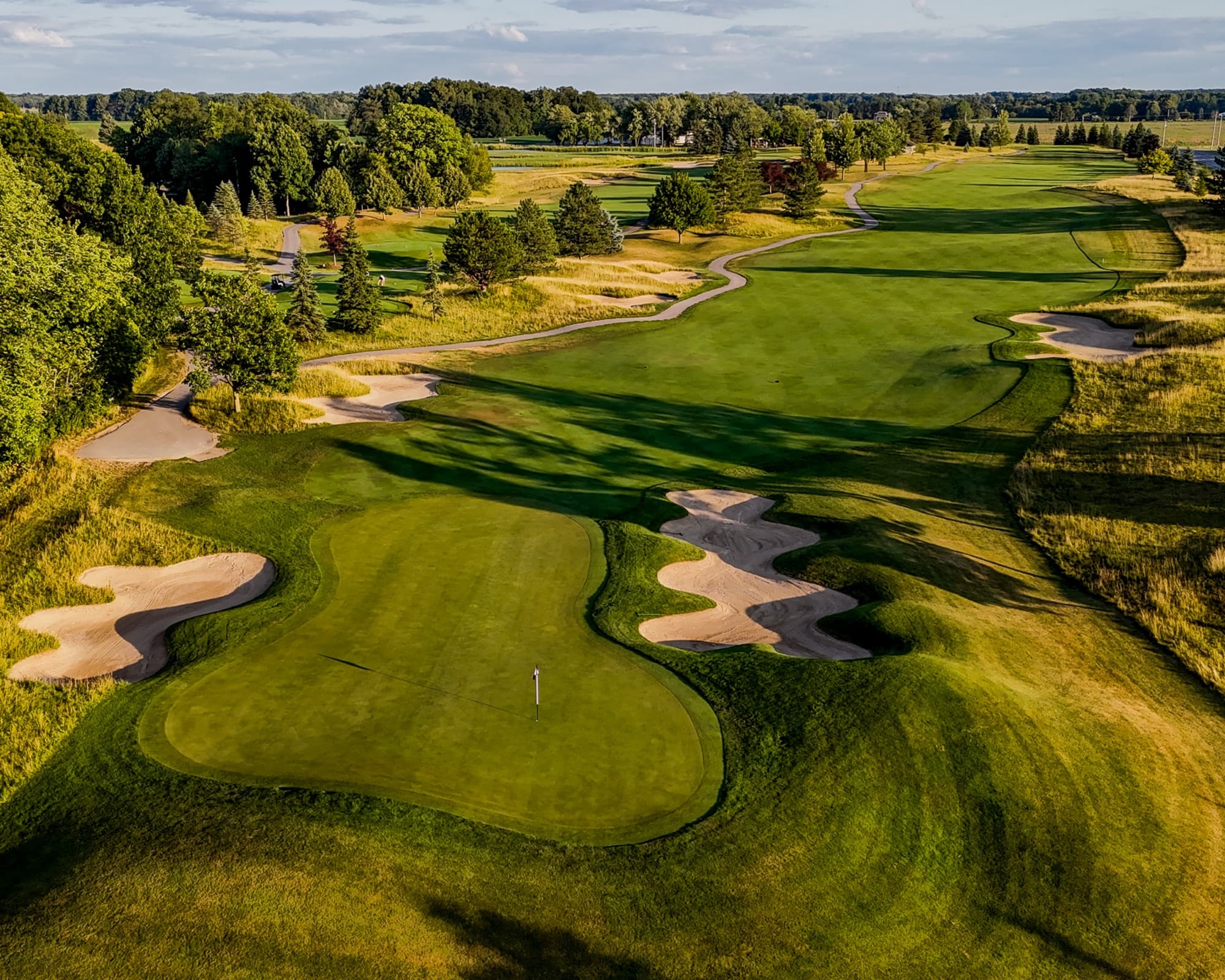 Aerial of the 14th green at The Fortress flanked by scalloped bunkers, a serpentine fairway bunker climbing toward open farmland